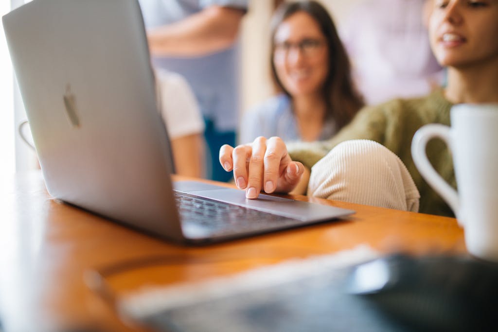A group of women casually collaborating on a laptop at a desk with a coffee mug.